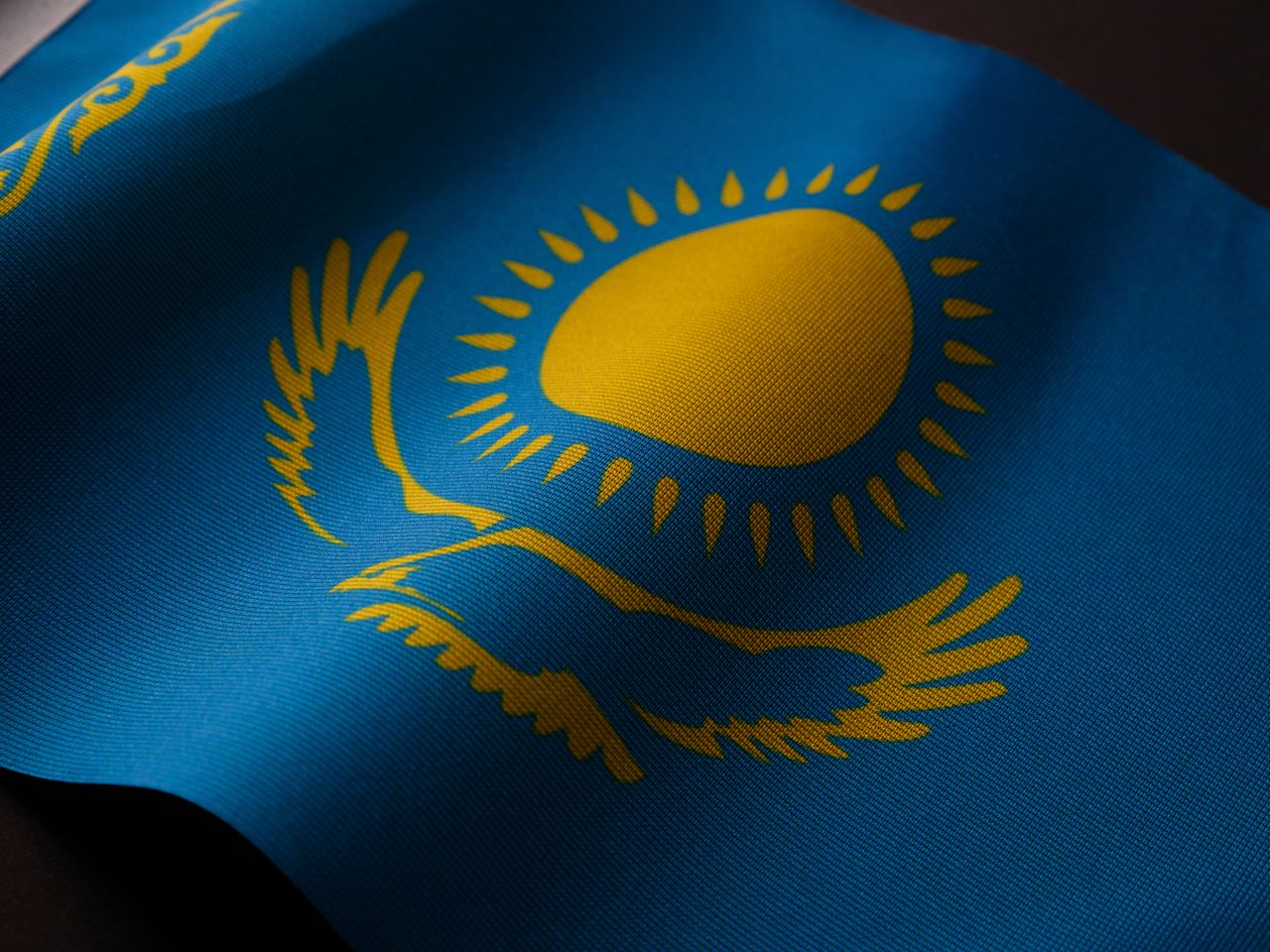 pexels-photo-16034032-16034032 Close-up of the Kazakhstan flag featuring a golden sun and eagle on a blue backdrop.